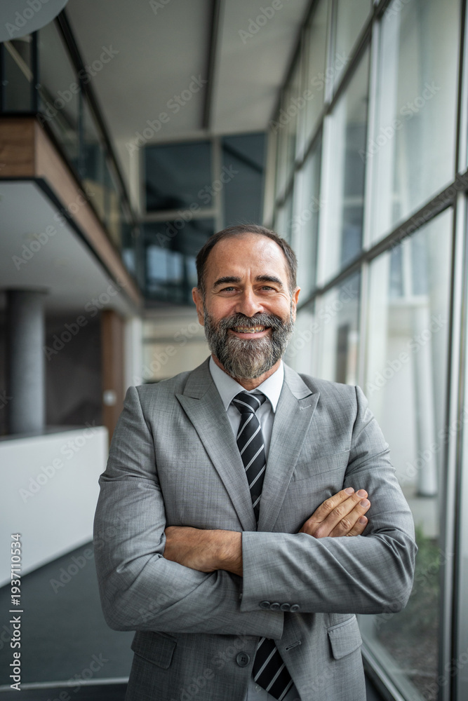 Fototapeta premium Senior businessman smiling with crossed arms in office corridor