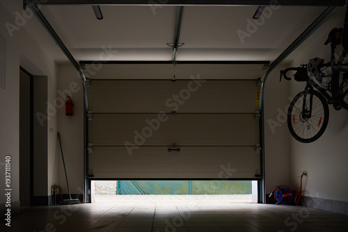 Interior view of residential garage with partially open sectional door, ceiling rails and bicycle