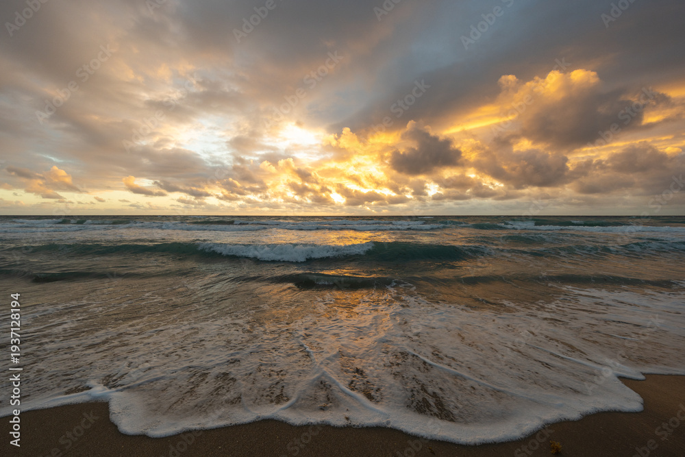 Obraz premium Dramatic ocean sunrise after storm with waves washing onto sandy beach
