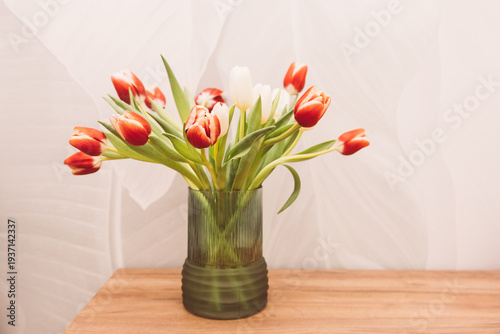 Bouquet of beautiful tulips in vase on wooden table against light green background
