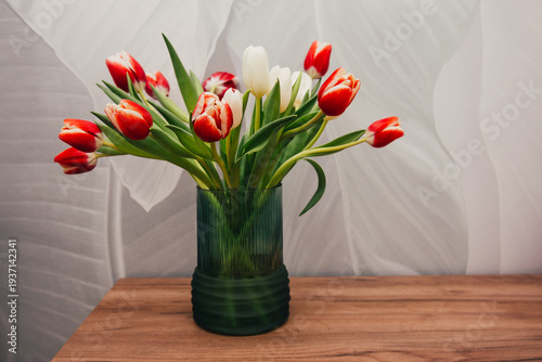 Bouquet of beautiful tulips in vase on wooden table against light green background