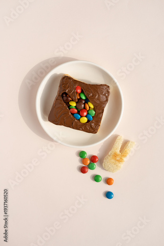 Toast with chocolate and nut paste, decorated with colored rabbit-shaped confects, on a white plate. Concept of a festive Easter breakfast, top view