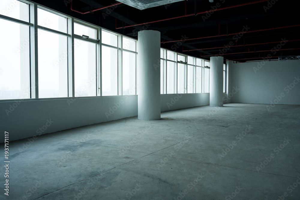 Fototapeta premium Empty office space with bare concrete floor, white columns, large windows and exposed ceiling infrastructure