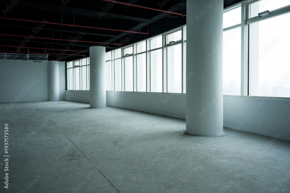 Fototapeta premium Empty office space with bare concrete floor, white columns, large windows and exposed ceiling infrastructure