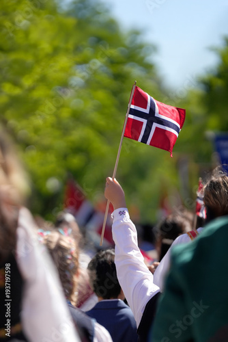 Happy people celebrating Norway's National Day by waving red, white, and blue Norwegian flags during a parade. Traditional Norwegian culture and pride.