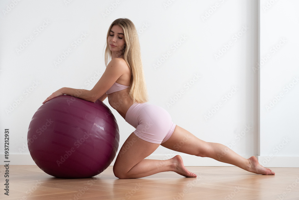 Naklejka premium Mujer joven apoyada en fitball burdeos con pierna estirada, pose de pilates elegante (formato horizontal)
