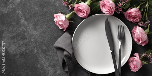 Table setting with a white plate, silverware, and pink roses as centerpiece.