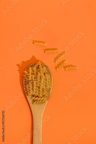 Raw pasta in spoon isolated on orange background, top view