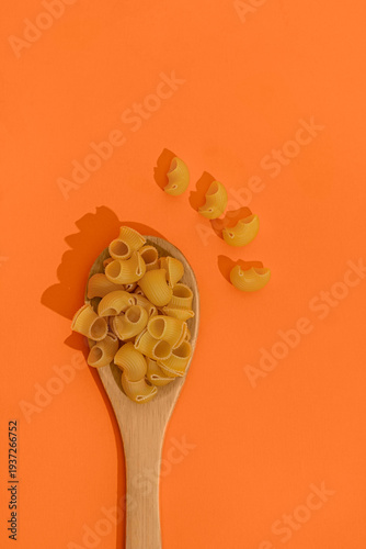 Raw pasta in spoon isolated on orange background, top view