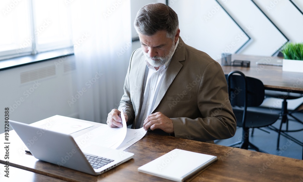 Fototapeta premium Mature businessman working with document in modern office, reading contract, analyzes graph