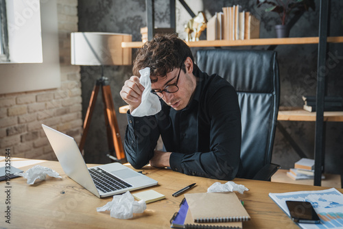 Man, tissue and sick by laptop in office with sneeze, allergy and virus infection on table. Business, health problem and male worker for cold, flu and fever symptoms in workplace for disease