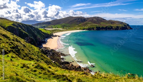 Lush coast featuring grassy hills meets a sandy beach and turquoise sea under a cloudy sky in a scenic panorama