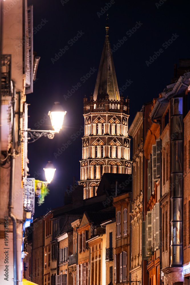 Fototapeta premium Bell tower of Saint-Sernin Basilica illuminated at night from Rue du Taur in Toulouse, Occitanie, France