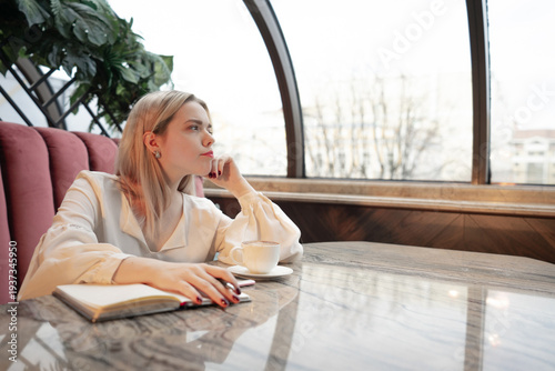 Dreamy young woman writing down future plans and goals in own diary and looking in window
