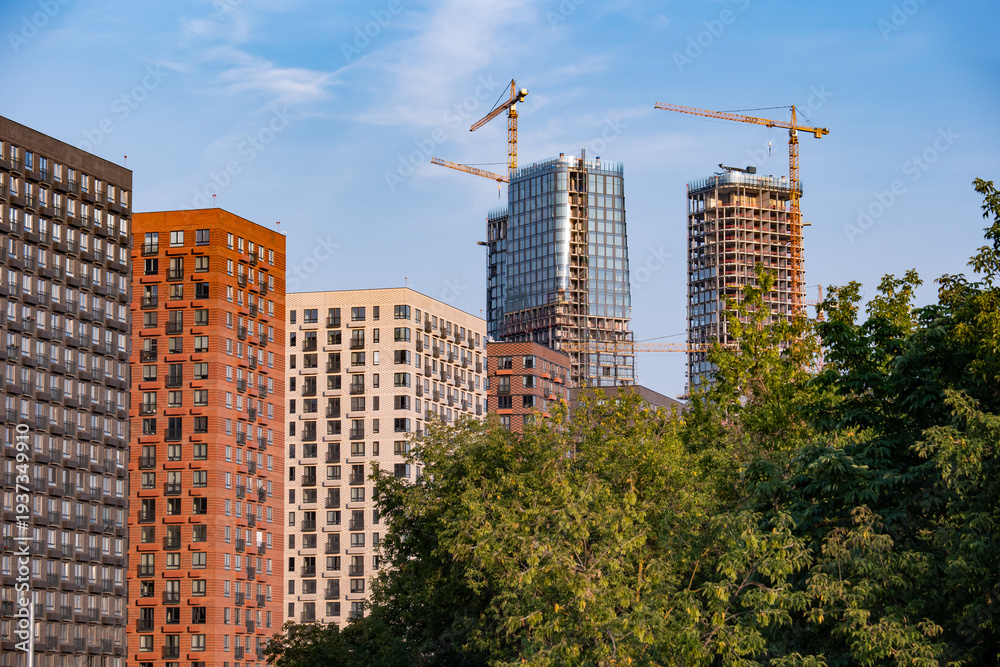 Fototapeta premium Urban cityscape with new residential towers rising above buildings, cranes on a blue sky
