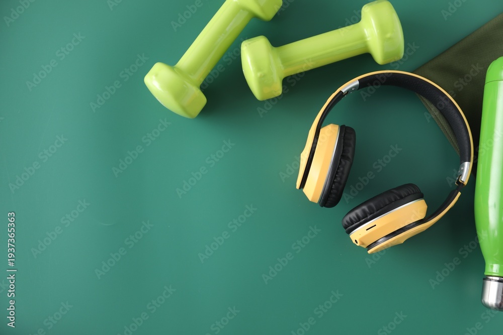 Naklejka premium Yellow headphones and dumbbells on green background, flat lay. Space for text