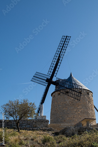 Historic stone windmill with large blades under clear blue sky.
