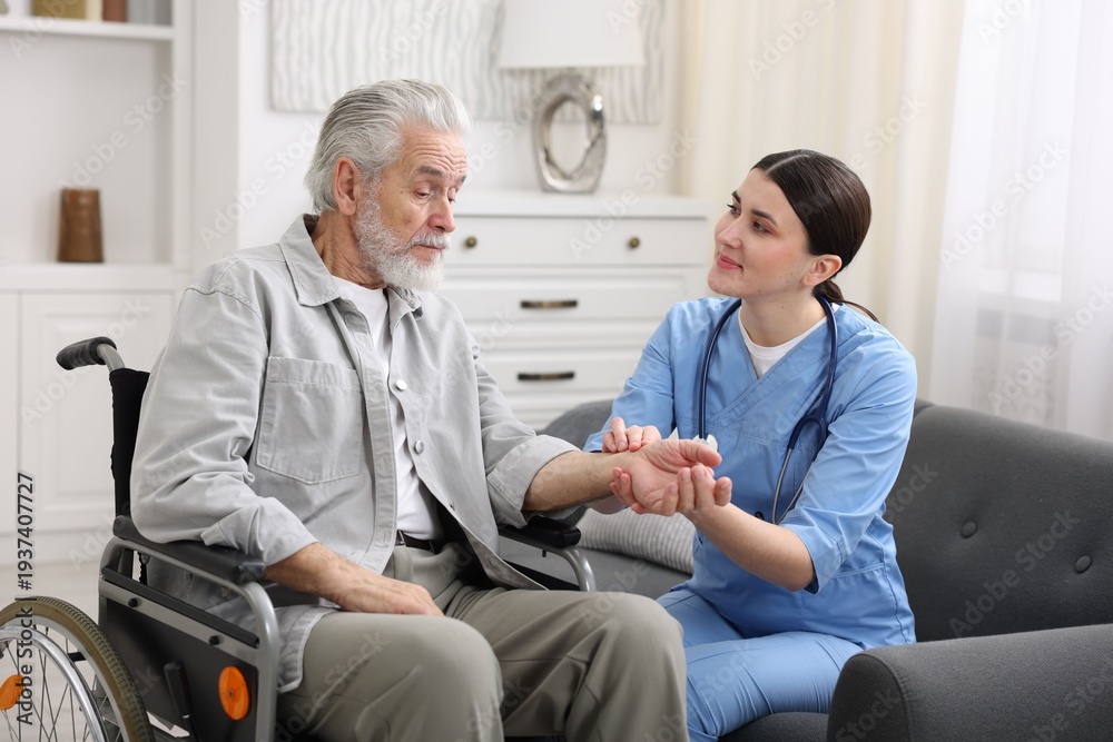 Obraz premium Care worker checking senior man's pulse in wheelchair indoors