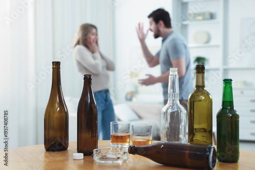 Drunk man abusing his wife at home, focus on different alcohol drinks and cigarette