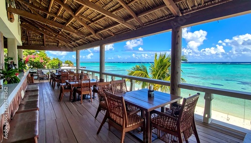 Outdoor restaurant terrace overlooking turquoise waters, with tables, chairs, and a thatched roof on a sunny day