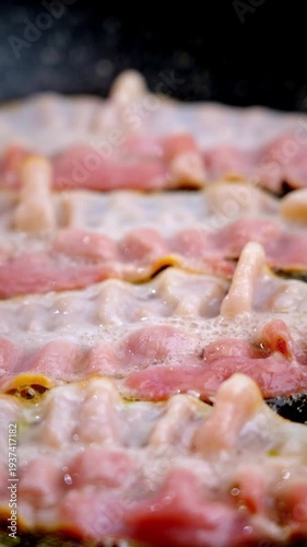 Sizzling raw bacon strips on skillet, prep cook prepping slices, pink fat bubbling, oil droplets shimmering, closeup texture evokes morning aroma