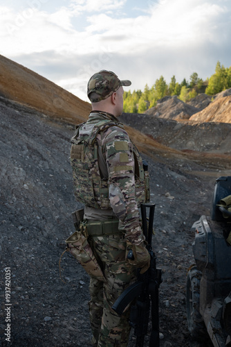 Armed Soldier Standing Near ATV in Rugged Quarry Landscape
