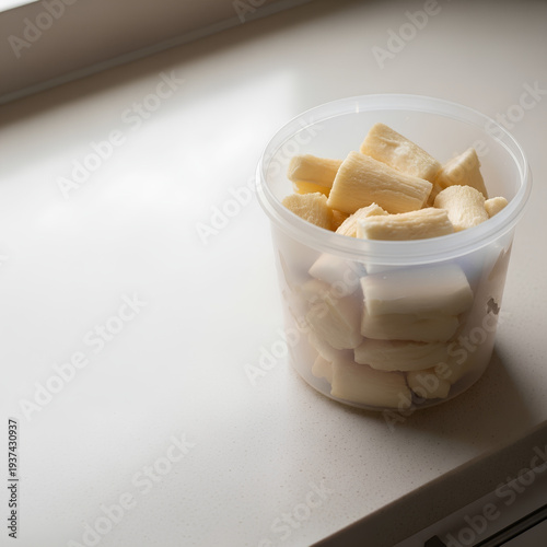 Plain plastic tub with fermented cassava pieces placed in the right third of a light beige countertop, large empty left side acting as negative space for cultural or fermentation copy.