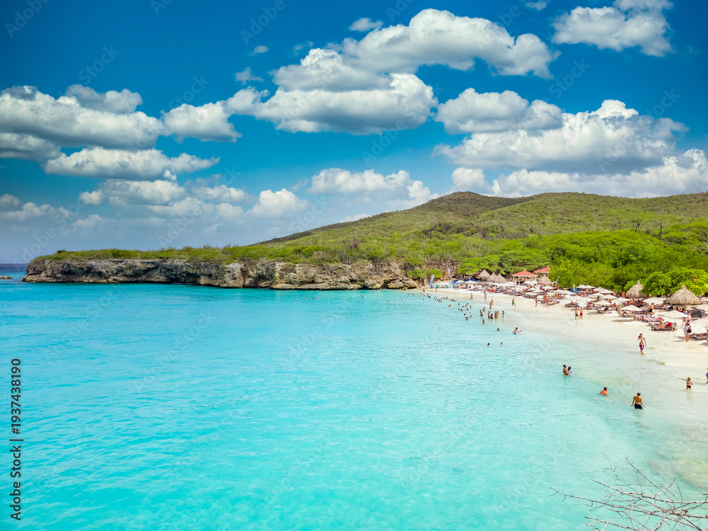 Obraz premium Aerial view of tourists enjoying the Grote Knip beach in Curacao turquoise water, palm trees, beach umbrellas 