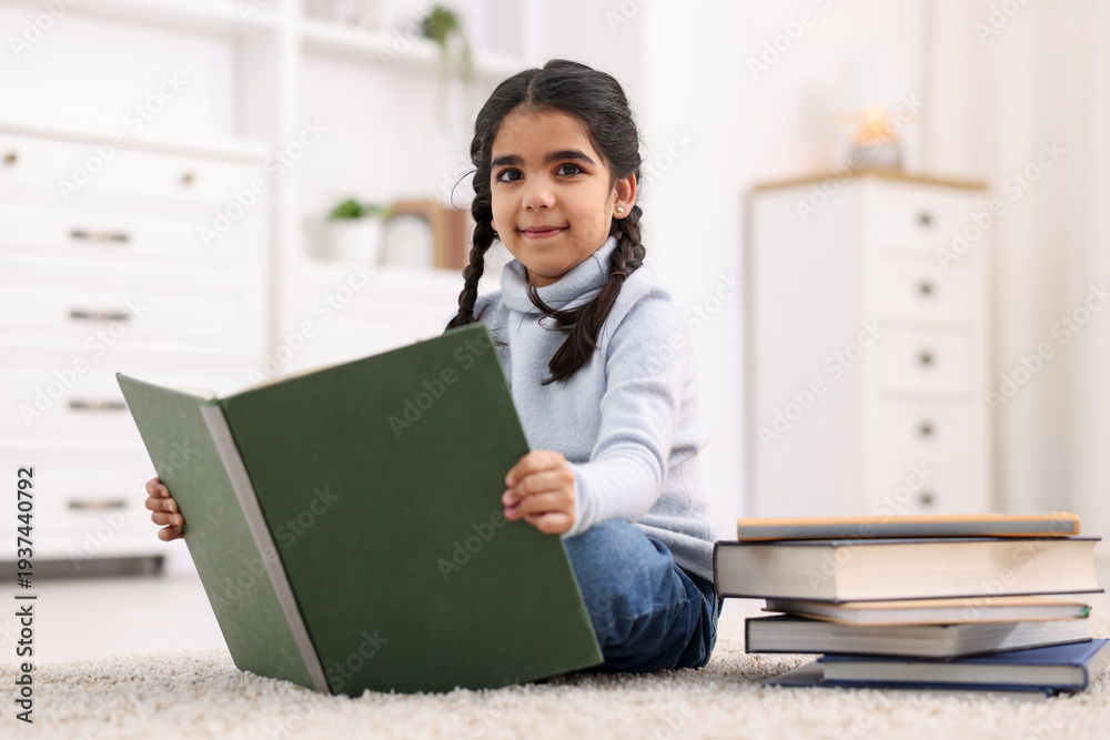 Naklejka premium Cute little girl reading book on floor at home