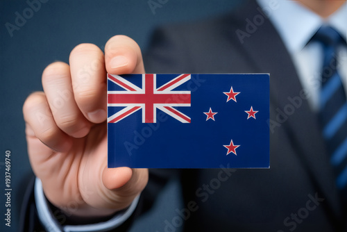 Elegant business professional proudly displaying New Zealand flag card, showcasing patriotism and international commerce appeal