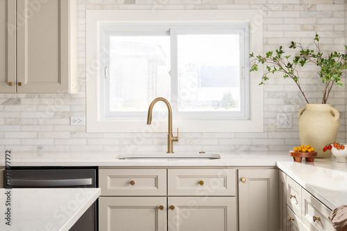 A kitchen detail with brown cabinets, marble subway tile backsplash, gold faucet, and decorations on the marble countertop.