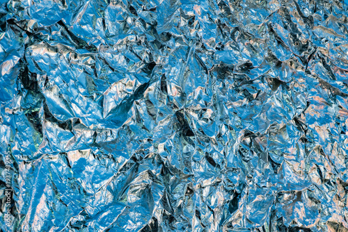 Shiny crumpled blue metallic foil reflecting light creating an abstract texture background