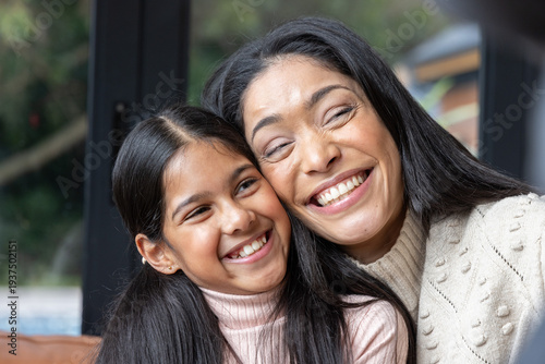 Mom and daughter sitting on couch by glass door smiling wearing knit sweater and ribbed turtleneck