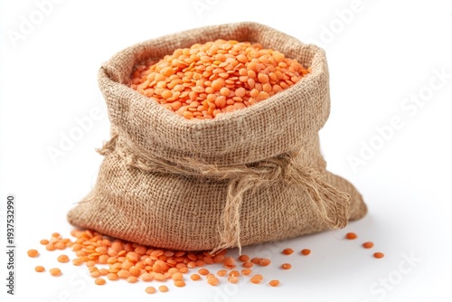 A burlap sack filled with red lentils sits on a white surface with some lentils spilled out around the base