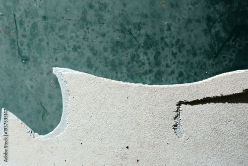 Close-up of chipped and cracked white plastic edge against dark green surface abstract textured background
