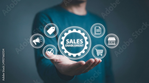 A persons hand holding a glowing digital representation of sales enablement with numerous business related ico