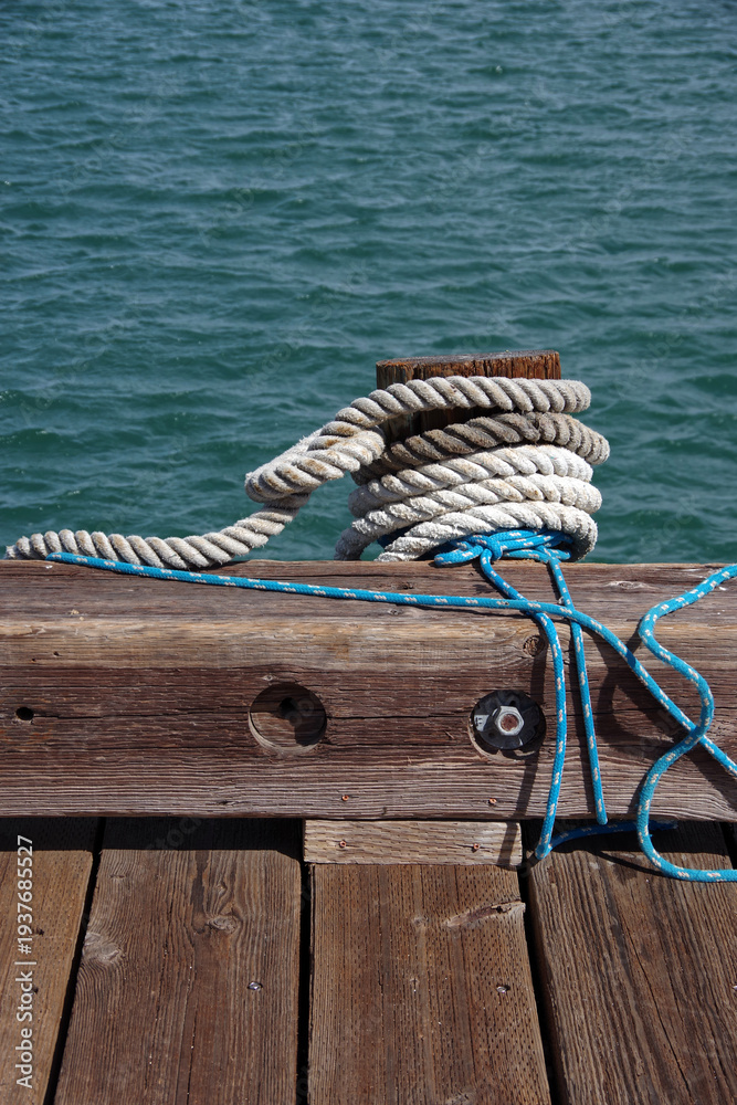 Fototapeta premium Heavy rope tied around a wooden post on a harbor pier