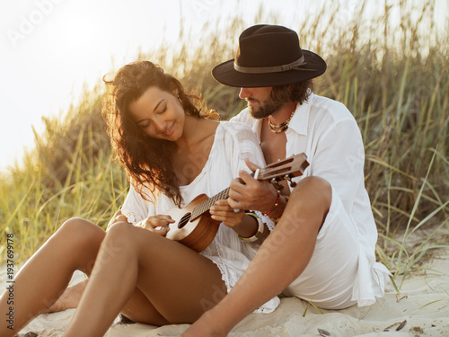 Tableau sur toile Boho Couple Playing Ukulele Together on Sandy Beach at Sunset in Summer Light