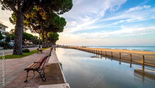 Scenic beach view with benches & trees along paved walkway, leading towards the soft ocean horizon under a bright sky