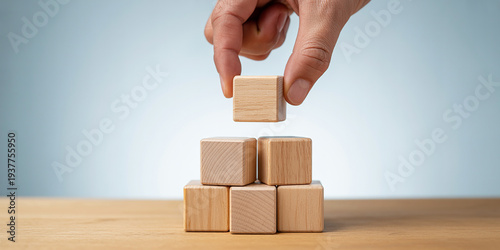 Hand placing a single wooden block on of a stacked pyramid of blocks on a table 