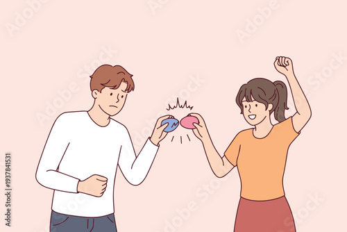 Young couple playing traditional egg tapping game on Easter day with boy losing as his egg gets a crack while girl celebrates victory and spring holiday custom