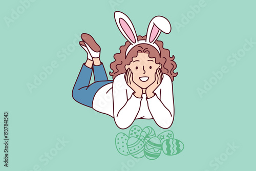 Little girl wearing bunny ears headband celebrating successful easter egg hunt with many decorated eggs on green floor during spring holiday fun and games