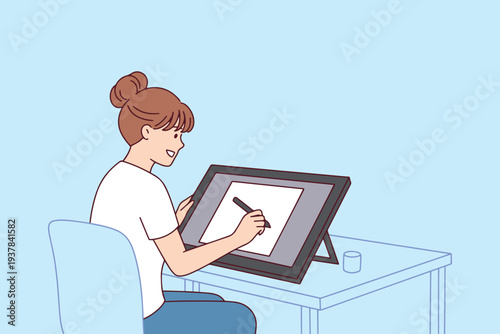 Professional female artist drawing on a digital graphics tablet in her studio working on creative project or digital illustration for online portfolio