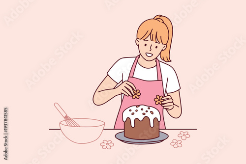 Young girl decorating traditional easter cake paska with fresh flowers in the kitchen preparing for religious holiday dinner and spring festive celebration