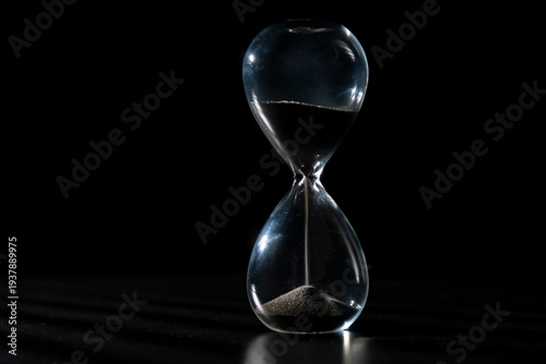 Hourglass shows flowing sand in dark background with light creating shadows
