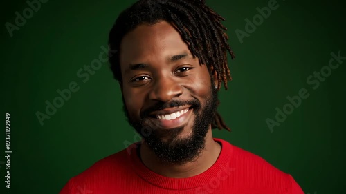 Smiling African American Man with Dreadlocks in Red Sweater Against a Dark Green Background Studio Portrait with Warm Lighting