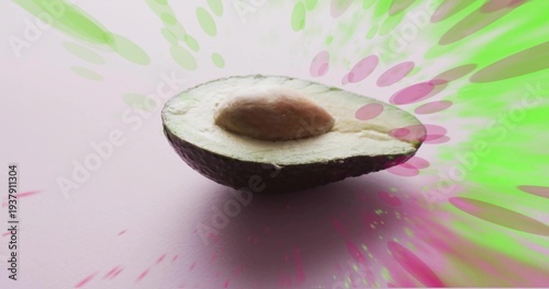 Resting halved avocado showing pale green flesh and brown pit on pastel pink, neon bursts