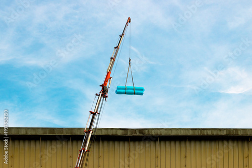 Foto Industrial telescopic crane lifting heavy cargo wrapped in blue plastic against a bright sky, construction site and heavy machinery concept