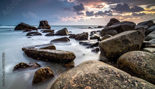 Rocky shore with long exposure ocean water under cloudy skies at sunrise/sunset, rocks in foreground