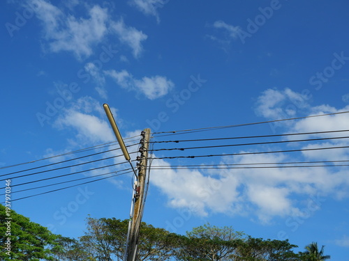 Streetlight pole and lamp with  white cloud and green tree on blue sky in background at Thailand, Old electrical wiring system